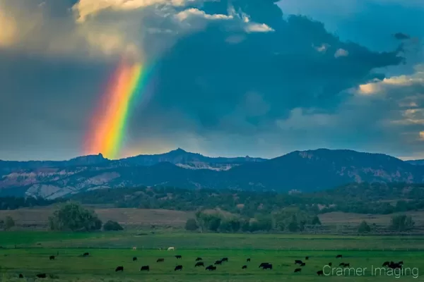 Cramer Imaging's fine art landscape photograph of a rainbow arc appearing over mountains and a rural cattle field in Utah