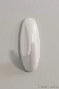 Photograph of a command strip brand white wall hook hanging on the white wall background by Cramer Imaging