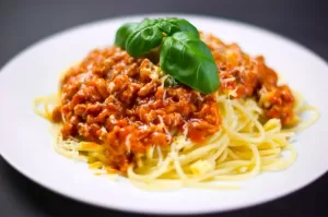 Photograph of a plate full of spaghetti with ragu sauce and basil leaves on top