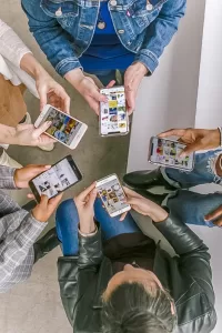 Photo of a group of 5 people standing in a circle holding their smart phones in the middle