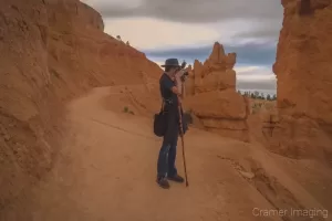 Professional landscape photographer Audrey Cramer standing on the Navajo trail of Bryce Canyon Utah getting a shot of the scene