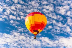 Fine art photograph of a warm-toned hot air balloon soaring in the sky with clouds in Panguitch, Utah by Cramer Imaaging