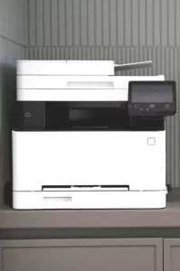 Photo of a 3-in-1 photocopy machine, printer, and fax machine sitting in a corner on a counter top