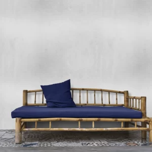 Photograph of an outdoor bench sitting against a gray wall with a blue pillow and cushion