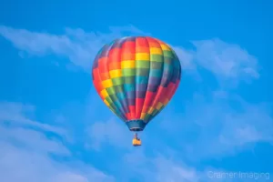 Cramer Imaging's fine art photograph of one colorful rainbow hot air balloon taking flight in Panguitch Utah with a blue morning sky