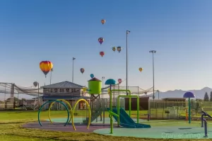 Cramer Imaging's fine art photograph of lots of hot air balloons taking flight in Panguitch Utah over playground equipment and a baseball field