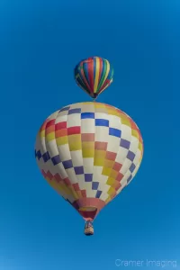 Cramer Imaging's fine art photograph of two colorful hot air balloons taking flight in Panguitch Utah with a blue morning sky