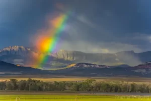 Cramer Imaging's fine art landscape photograph of a broken rainbow with light streaks against moody storm clouds over a field in Panguitch, Utah