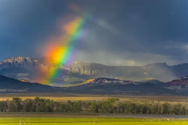 Cramer Imaging's fine art landscape photograph of a broken rainbow with light streaks against moody storm clouds over a field in Panguitch, Utah