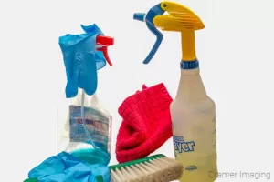 Cramer Imaging's photograph of cleaning chemicals in spray bottles, disposable blue gloves, a red rag, and a duster