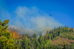 Cramer Imaging's landscape photograph of a helicopter flying over a wildfire to dump water from a suspended bucket