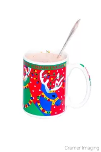 Photograph of a colorful Christmas-themed mug of hot chocolate with a spoon by Cramer Imaging