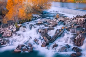 Fine art landscape photograph of the Idaho Falls waterfall with logs, rocks, and autumn leaves by Cramer Imaging