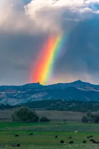 Cramer Imaging's fine art landscape photograph of a rainbow appearing over an idyll or rural landscape with cows in Utah