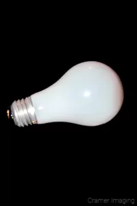 Photograph of a single incandescent light bulb on its side on a black background by Cramer Imaging