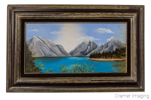 Cramer Imaging's photograph of a framed landscape painting with mountains and a lake on a white wall