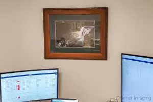 Photograph of Cramer Imaging's fine art photograph 'Upper Mesa Falls' on the wall of a room with a desk and computer