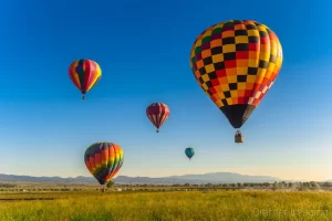 Fine art photograph of a small cluster of hot air balloons flying over a farm field in Panguitch, Utah by Cramer Imaging