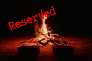 Graphic of a roaring campfire at night with 2 seats in front with a red reserved stamp across it