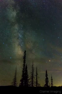 Cramer Imaging's fine art astrophotography photograph of the Milky Way in the night sky with clouds and trees in silhouette