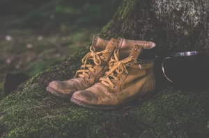 Photograph of used hiking boots sitting in moss with a cup