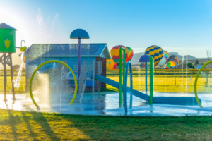 Cramer Imaging's fine art photo of an active splash pad with hot air balloons in the background