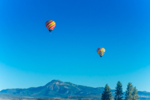 Cramer Imaging's fine art photo of 2 hot air balloons flying in the sky with mountains and trees